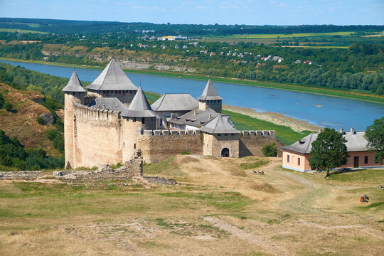 Historic medieval fortress and church overlooking a winding river and rural landscape under a bright blue sky.