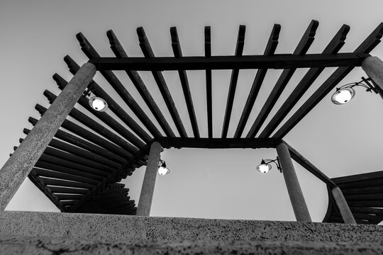 Black and white low angle architectural perspective of modern wooden pergola structure with lamps