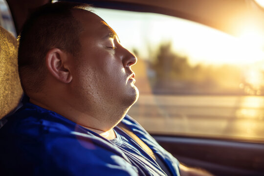 A person sits in a car seat with eyes closed. The sun is setting in the background, creating a warm glow outside the vehicle