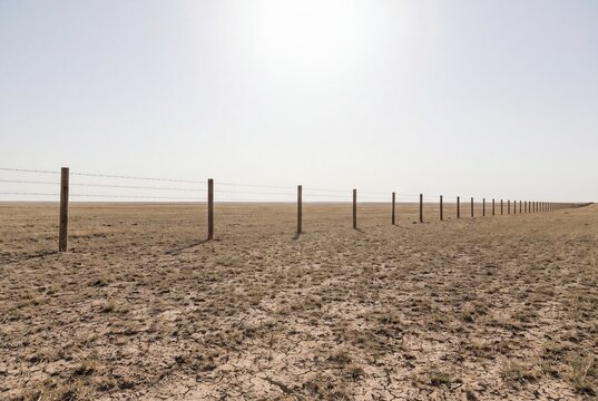 Barbed wire fence in dry cracked soil prairie wilderness landscape