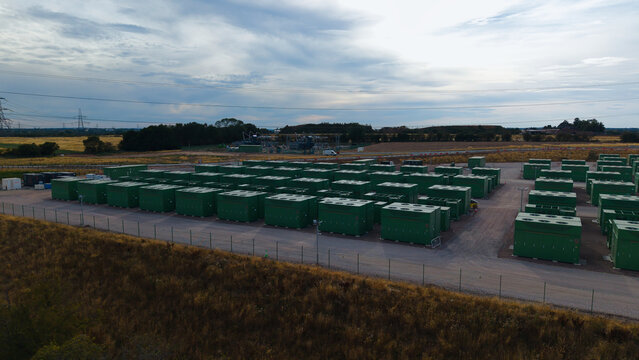 Aerial view of a large-scale battery energy storage system facility with rows of green containers for grid resilience and power management in Birmingham, England, United Kingdom.