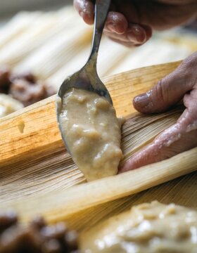 Hands spreading masa on corn husk crafting traditional tamale celebrating latin american culinary heritage and cultural traditions in food preparation