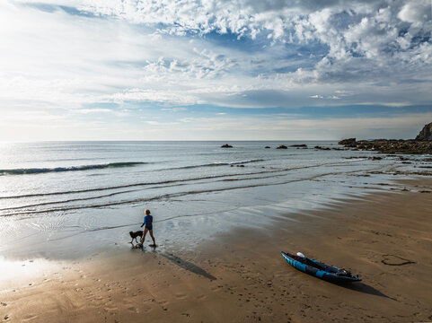 Woman and dog with kayak on Beach from a drone,  North Devon and Cornwall Coastpath Border from a drone, Welcombe Mouth Beach, Devon, Cornwall, England