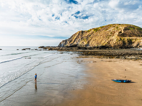 Woman with kayak on Beach from a drone,  North Devon and Cornwall Coastpath Border from a drone, Welcombe Mouth Beach, Devon, Cornwall, England