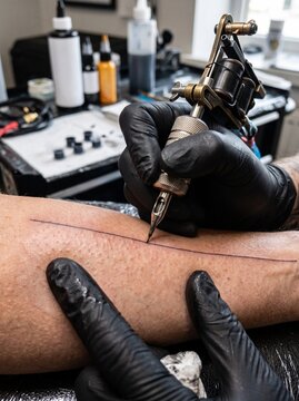 Professional tattoo artist drawing a black line on skin