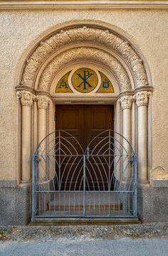 Kunstvoll gestaltetes Eingangportal mit Archivolte, Christusmonogramm und Ziergitter an der Kirche der Katholisch-Apostolischen Gemeinde in Berlin-Neuk&ouml;lln (Ansicht von Norden)