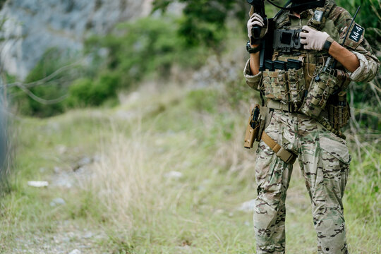 Determined soldier standing in camouflage uniform with tactical gear, displaying resilient and confident emotion in nature