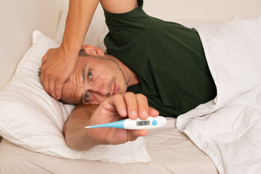 Sick Man Showing High Fever Reading on Digital Thermometer in Bed