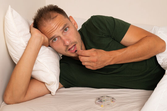 Man Taking Daily Medication from Weekly Pill Organizer in Bed