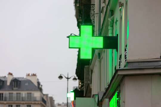 Illuminated Green Pharmacy Cross Sign on Urban Building