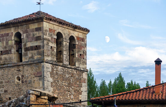 Historic bell tower of Santos Justo y Pastor church in Ruesga with daytime moon, Palencia Spain.