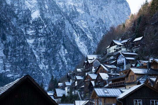 View of traditional wooden houses nestled on steep hillside in Hallstatt, Austria, surrounded by majestic snow covered Alpine mountains in winter. Cold snow covered village in Austria.