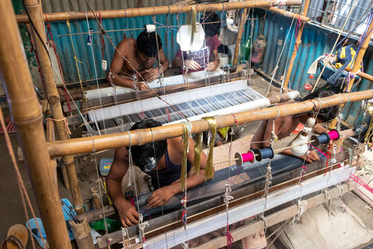Narayanganj, Bangladesh - 29 August 2021: View of traditional Jamdani Saree weavers working at a wooden loom with colorful threads in a workshop.
