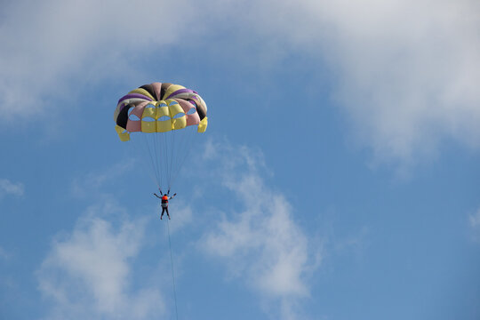 Cox's Bazar, Chittagong Division, Bangladesh - 18 August 2023: View of a person parasailing high in the blue sky with a colorful parachute.