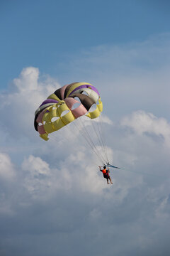 Cox's Bazar, Chittagong Division, Bangladesh - 18 August 2023: View of a person parasailing with a colorful parachute against a blue sky with white clouds.