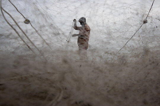 Cox's Bazar, Bangladesh - 16 August 2023: View of a fisherman working with a large fishing net under an overcast sky.