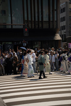 Taito City, Japan - 15 May 2026: View of people in traditional kimono crossing the street near Asakusa with modern buildings in the background.