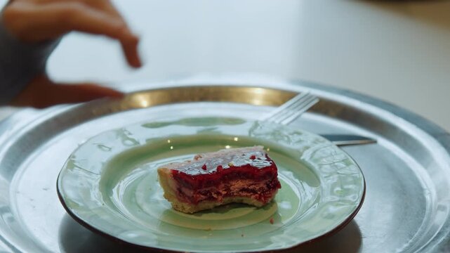 Close up of hand placing and adjusting pieces of red topped dessert on empty green plate with fork set against soft lighting in calm indoor environment