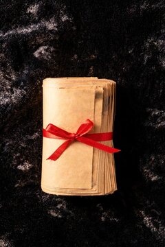 Rolled bundle of blank paper bills tied with red ribbon on dark velvet texture