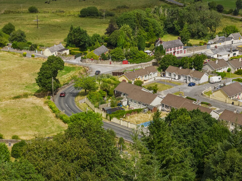 Aerial view of St Patrick's Church surrounded by residential houses, green fields, and winding roads in Portlaw, County Waterford, Ireland.