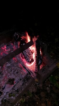 Burning wood logs in fire pit in dark style in red and orange colors representing outdoor camping and relaxation