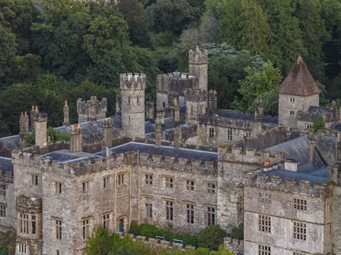 Aerial view of Lismore Castle with its historic stone towers, battlements, and surrounding lush green trees in Lismore, County Waterford, Ireland.