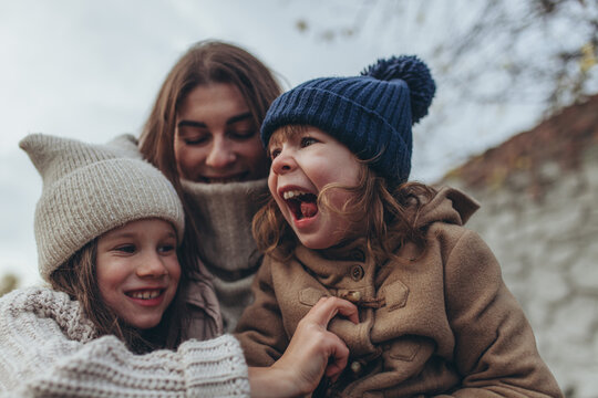 Mother laughing and playing with her two young daughters outdoors in autumn. Family love, bonding, childhood innocence, maternal warmth.