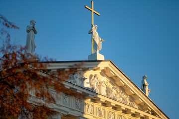 Fototapeta premium Autumn branches in warm evening light with Vilnius Cathedral in the background. Historic neoclassical architecture in Vilnius, Lithuania, photographed at golden hour.
