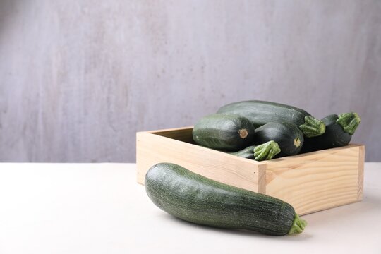 Fresh raw zucchinis in wooden crate on light table against gray background. Space for text