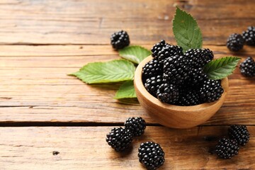 Ripe blackberries in bowl with leaves on wooden table, closeup. Space for text © New Africa