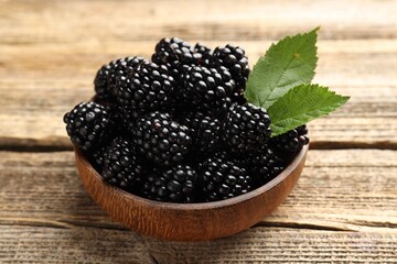 Ripe blackberries in bowl with leaves on wooden table, closeup © New Africa