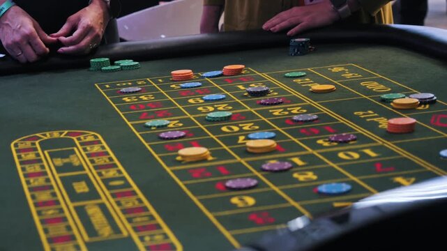 Hands place chips on numbered casino betting table with clear marker, scattered stacks, 