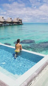 Luxury resort travel vacation destination idyllic overwater bungalow villa woman relaxing in infinity pool. Raw unedited vertical video of real unretouched woman model without any makeup