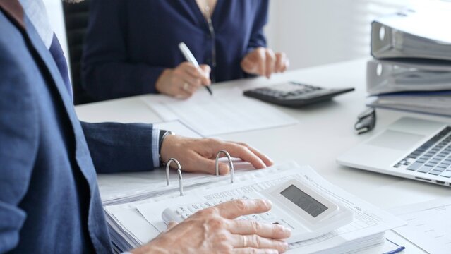 Close up of male accountant hands using calculator and collaborating with female colleague in a modern office, calculating taxes and analyzing financial data. Audit and taxes in business
