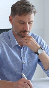 Businessman wearing blue sleek shirt is thinking and concentrating while working at the desk in a bright, modern office, demonstrating professionalism and efficiency. Business people concept