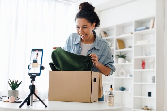 Excited Young Caucasian Woman Unboxing Package At Home, Smiling And Showing Joyful Emotion While Engaging With Camera. Bright Indoor Setting Portraying Positive Lifestyle And Consumer Experience.