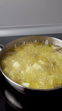 Diced potatoes for patatas bravas frying with olive oil in a frying pan on a ceramic stove