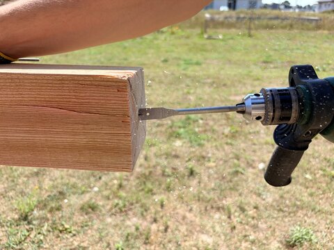 A power drill with a spade bit drilling into a wooden beam outdoors. Carpentry, construction, DIY woodworking
