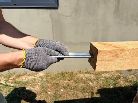 A builder uses a ruler to measure a threaded metal rod inserted into a wooden beam.