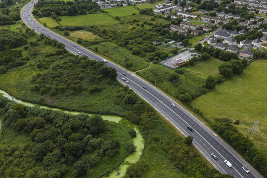 Aerial view of the N4 highway winding through lush green fields and near residential housing in Collooney, County Sligo, Ireland.
