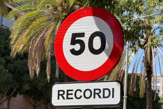 50 km/h speed limit sign with Catalan reminder plate on a palm-lined street in Catalonia, Spain