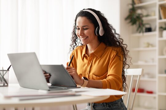Smiling Young Hispanic Woman Engaged In Work On Digital Tablet While Sitting At Desk In Home Office, Showing Focus And Determination. Office Environment And Business Concept.