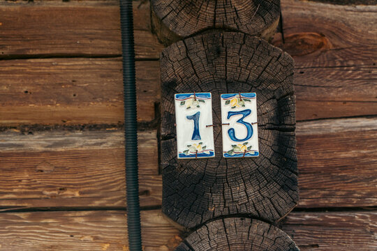 A close-up shot features ceramic tiles showing the house number 13 with blue digits and floral patterns mounted on an end-grain wooden log wall.