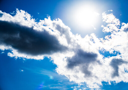 A bright sun shines through dramatic white and dark clouds against a clear blue sky.