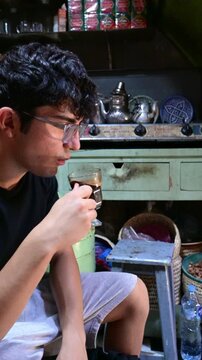 Marrakech, morocco. August 8, 2026. Young tourist with glasses drinking a traditional hot moroccan mint tea inside a souk shop in the marrakech medina. Slow motion video