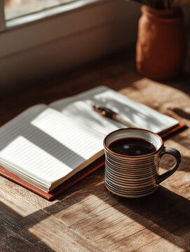 Coffee mug and notebook on wooden table enjoying sunlight