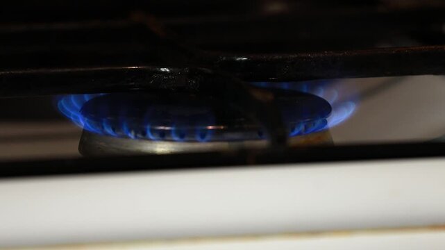 A close-up shot of a gas stove with a blue flame burning brightly