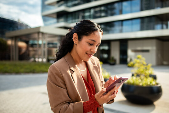 Smiling businesswoman using smartphone outside modern office