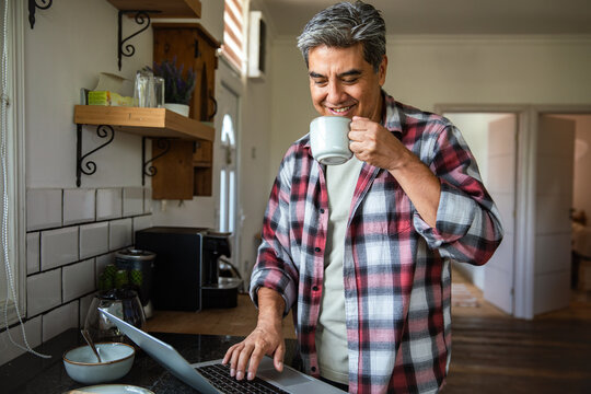 Middle-aged man working on laptop with coffee in home kitchen