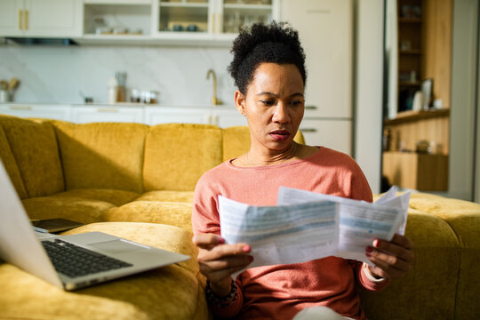 Concerned woman reviewing household bills with laptop at home
